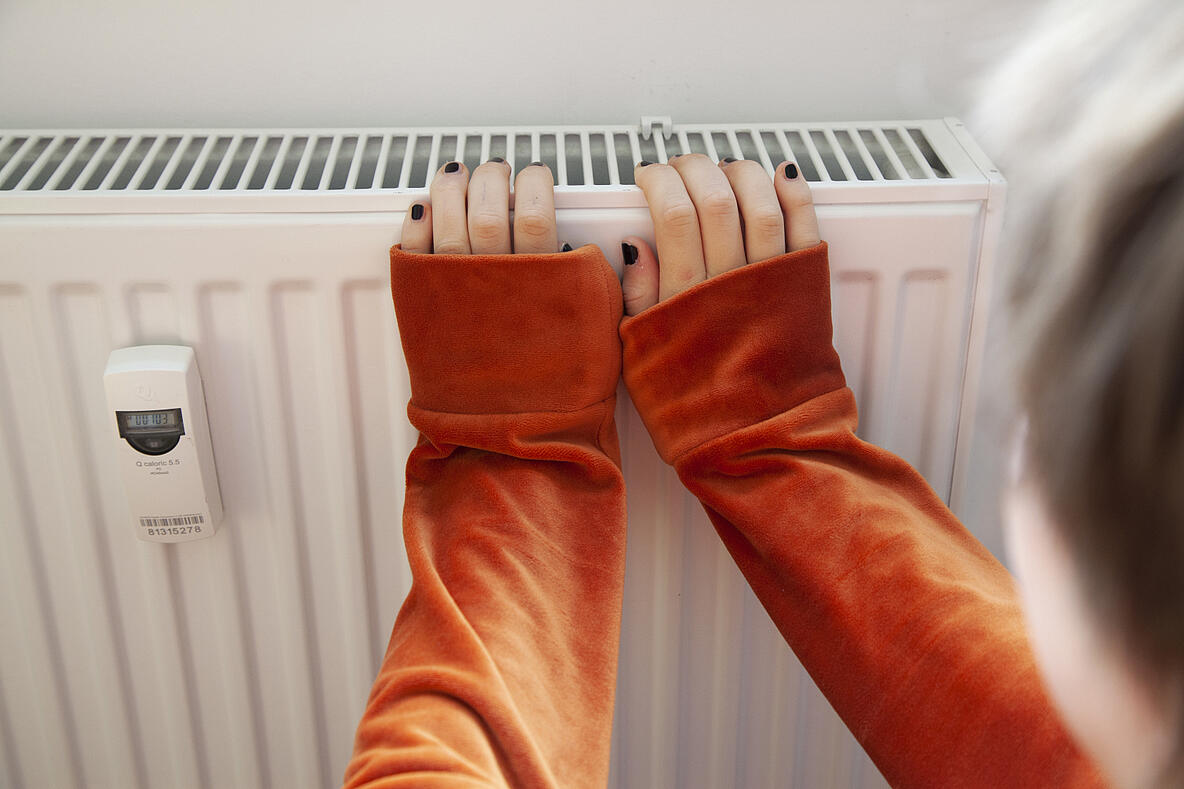 Person die sich mit ihren Händen an einer Heizung wärmt