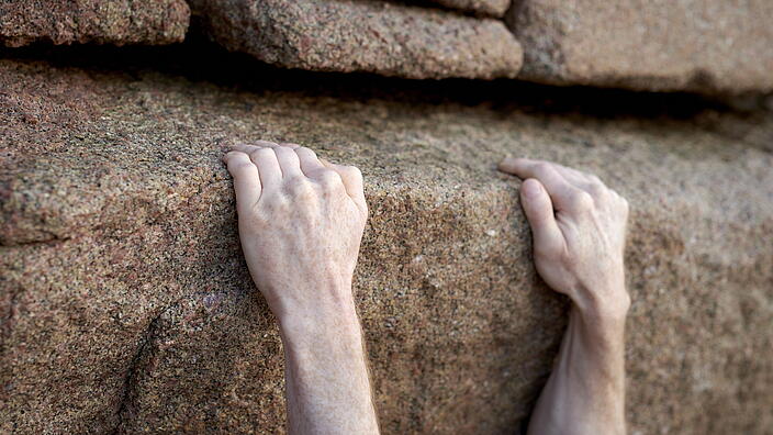 Hände die sich an Steinen festhalten.