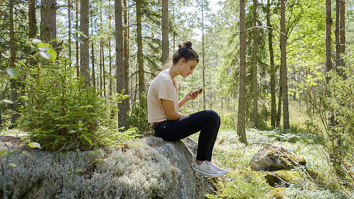 Person die im Wald aufs Smartphone schaut