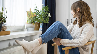 Frau auf einem Stuhl hat die Füße auf der Heizung abgestellt