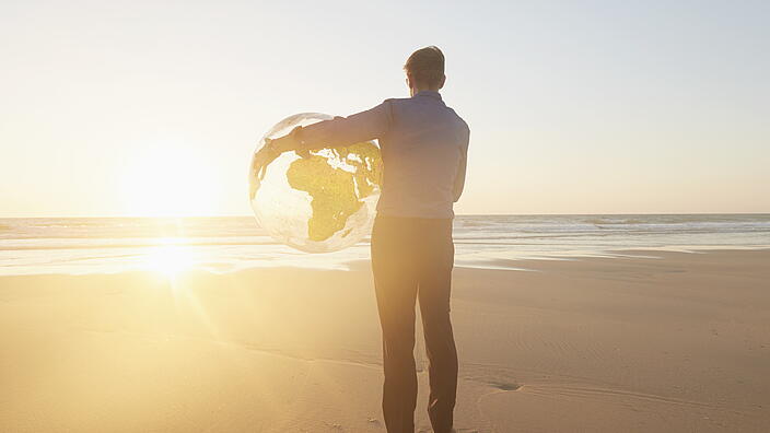 Mann der einen Globus am Meer hält