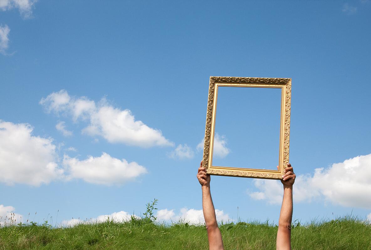 Arme die einen Bilderrahmen in die Luft vor dem Himmel halten