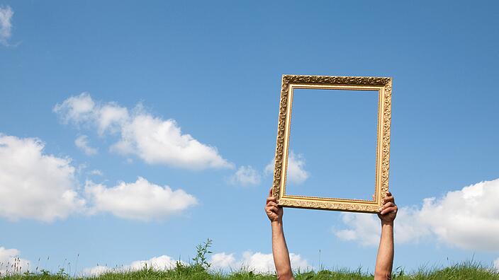 Arme die einen Bilderrahmen in die Luft vor dem Himmel halten