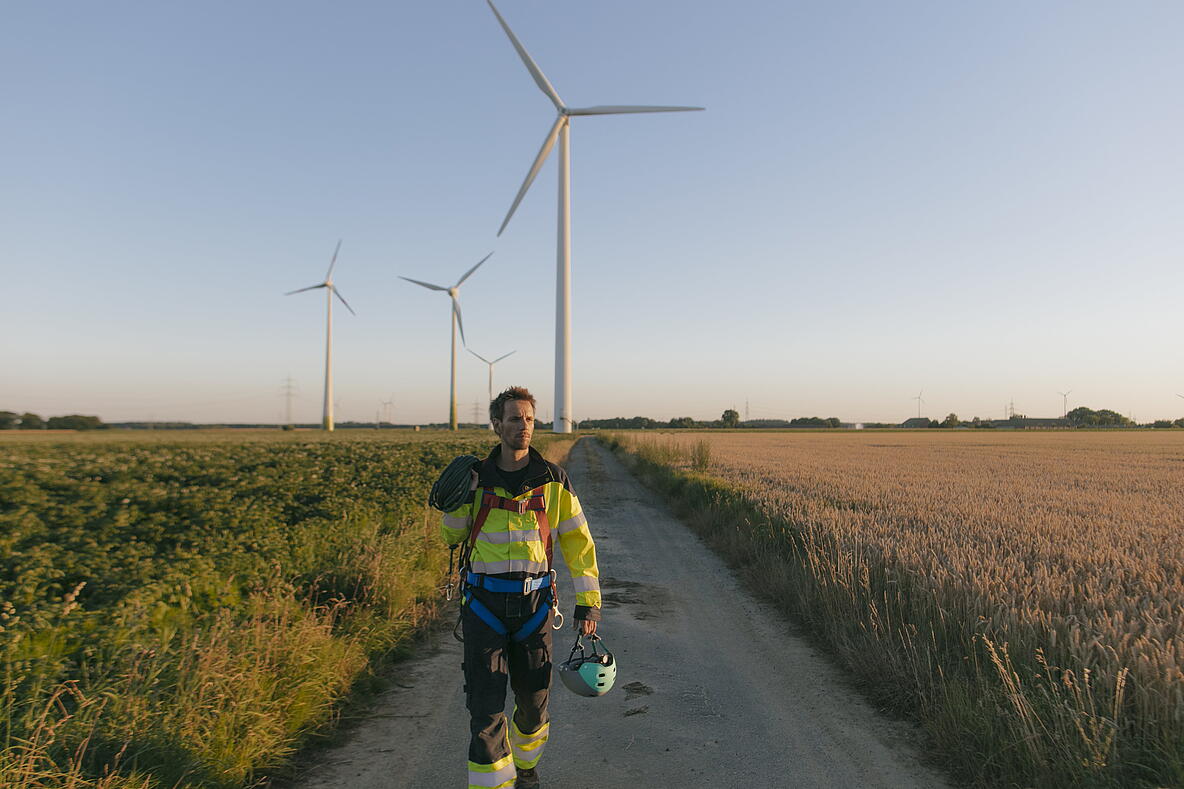 Person in Arbeitskleidung läuft den Weg zu Windrädern
