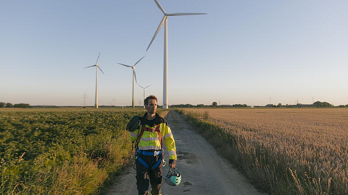 Person in Arbeitskleidung läuft den Weg zu Windrädern