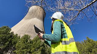 Kühlturm eines Kernkraftwerks vor blauem Himmel, ein Mensch steht davor und schaut nach oben