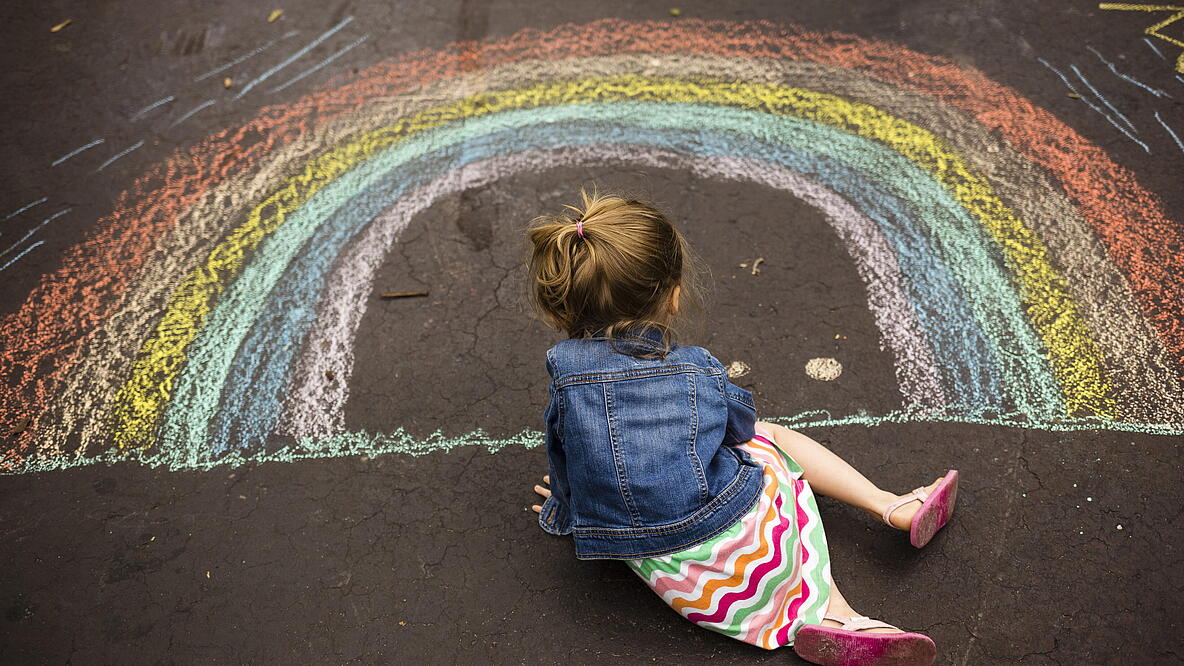 Kind das mit Kreide einen Regenbogen auf die Straße malt