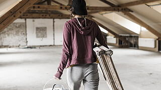 Person mit Leiter und Farbeimer auf einem Dachboden